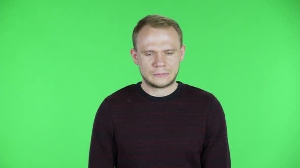 O retrato de um homem de meia-idade ouve a informação, olha para a câmera, está muito chateado e olha para baixo com culpa. Homem sem barba em camisola preta vermelha posando na tela verde no estúdio. Fechar. — Vídeo de Stock