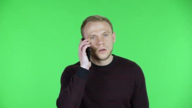 Öfke ve kızgınlıkla akıllı telefonda konuşan orta yaşlı bir adamın portresi. Siyah kırmızı kazaklı traşsız bir erkek stüdyoda yeşil ekranda poz veriyor. Kapat..