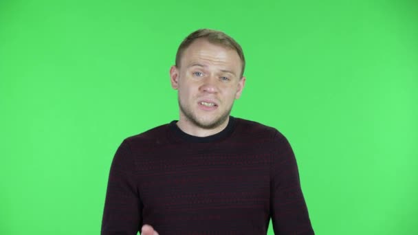 Porträt eines verwirrten Mannes mittleren Alters, der mit den Schultern zuckt. Unrasierter Mann im schwarz-roten Pullover posiert auf einer grünen Leinwand im Studio. Nahaufnahme. — Stockvideo