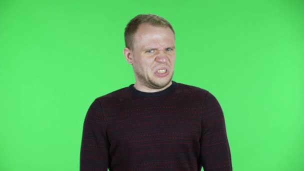 Retrato de un hombre de mediana edad mirando a la cámara con asco. Hombre sin afeitar en un suéter rojo negro posando en una pantalla verde en el estudio. De cerca.. — Vídeos de Stock