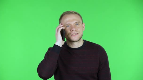 Retrato de um homem de meia-idade falando em um smartphone com indignação e irritação. Homem sem barba em uma camisola preta vermelha posando em uma tela verde no estúdio. Fechar. — Vídeo de Stock