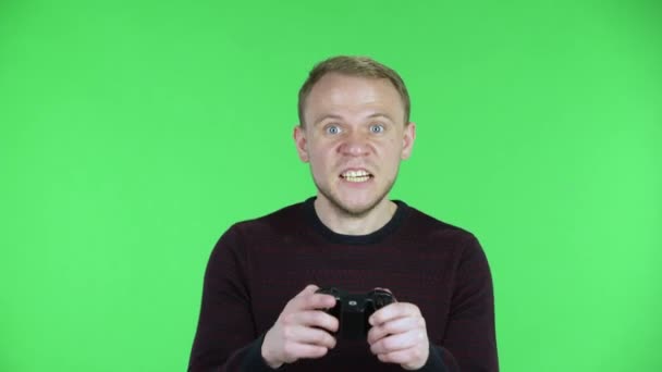 Portret van een man van middelbare leeftijd die een videospel speelt met behulp van een draadloze controller, verliest en is erg van streek. Ongeschoren mannetje in een zwarte rode trui poserend op een groen scherm in de studio. Sluiten.. — Stockvideo