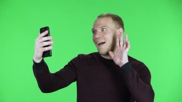 Porträt eines Mannes mittleren Alters, der mit Freude und Freude per Videoanruf auf dem Smartphone spricht. Unrasierter Mann im schwarz-roten Pullover posiert auf einer grünen Leinwand im Studio. Nahaufnahme. — Stockvideo