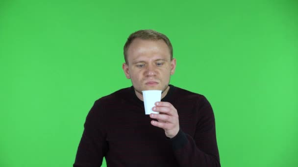 Portrait of a middle aged men drinking unpalatable coffee and is disgusted. Unshaven male in a black red sweater posing on a green screen in the studio. Close up. — Stock Video