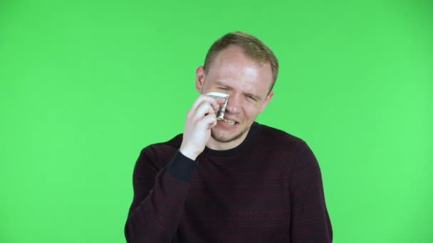 Retrato de un hombre de mediana edad llorando y limpiando lágrimas con un billete de un dólar. Hombre sin afeitar en un suéter rojo negro posando en una pantalla verde en el estudio. De cerca.. — Vídeos de Stock