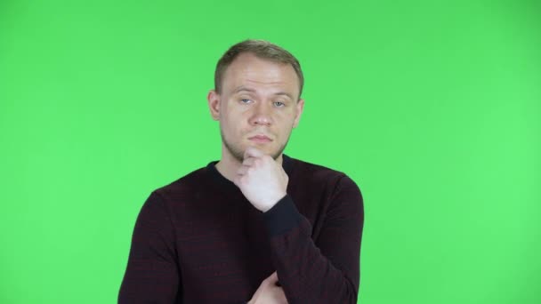 Porträt eines Mannes mittleren Alters, der in die Kamera blickt und konzentriert denkt. Unrasierter Mann im schwarz-roten Pullover posiert auf einer grünen Leinwand im Studio. Nahaufnahme. — Stockvideo