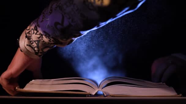 O carte deschisă se află pe o masă într-un studio întunecat sub lumina reflectoarelor. Omul închide cartea şi o ia. Nu există un prieten mai degrabă decât o carte. Mişcare lentă. Close up . — Videoclip de stoc