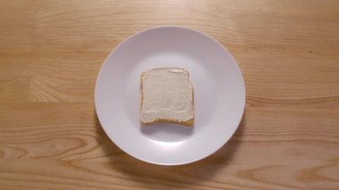 Farklı malzemelerden sandviç yapma süreci. Hareket animasyonunu durdur. Üst Manzara. Taze ekmek, tereyağı, marul, domates, salatalık, jamon ve peynir beyaz tabakta görünür. Kapat..
