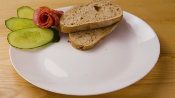 バター、ソーセージ、チーズ、サラダと新鮮なパンのおいしいサンドイッチは白いプレートに落ちます。子供と大人のための朝の健康的な食事のコンセプト。閉めろ。スローモーション. — ストック動画