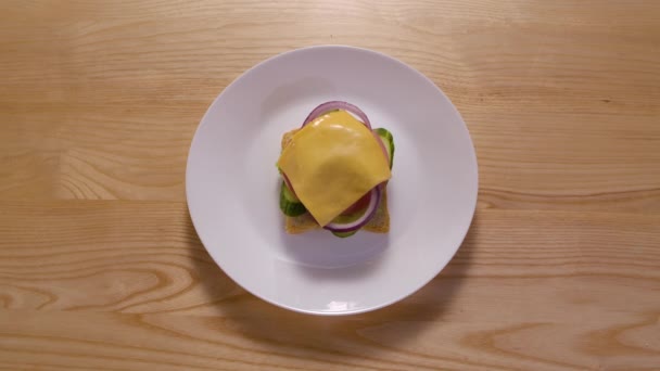 Leckere Sandwich-Essen Animation aus verschiedenen Zutaten. Stop-Motion-Animation. Ansicht von oben. Frisches Brot, Salat, Tomaten, Gurken, Wurst, Zwiebelringe und Käse auf weißem Teller. Nahaufnahme. — Stockvideo