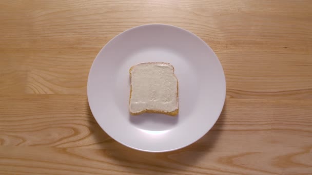 Proceso de elaboración de sándwich a partir de diferentes ingredientes. Detener la animación en movimiento. Vista superior. Pan fresco, mantequilla, lechuga, tomates, pepinos, jamón y queso aparecen en el plato blanco. De cerca.. — Vídeos de Stock
