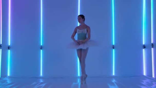 Profi balerina tánc balett A stúdióban hátterében sokszínű neon csövek. Egy színpadi ruhás lány táncot jár, és kecsesen ugrik. Közelről.. — Stock videók