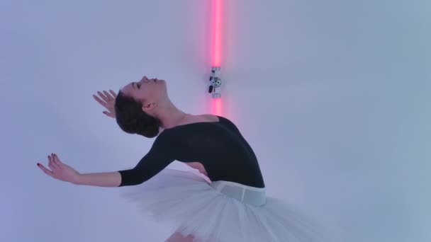 Una ballerina professionista mostra bellissime mosse di danza in studio sullo sfondo di tubi al neon multicolore. La ballerina muove le braccia con grazia e si piega dolcemente. Chiudete. Rallentatore. — Video Stock