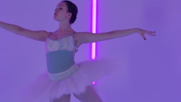 Profi balerina tánc balett A stúdióban hátterében sokszínű neon csövek. Egy színpadi ruhás lány kecses pas-t gyúr kezeivel és ugrik. Lassú mozgás. Közelről.. — Stock videók