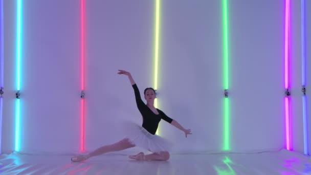 Una bailarina en el estudio sobre el fondo de tubos de neón demuestra su flexibilidad, doblándose en su espalda, se inclina y acostada sobre sus pies, luego de pie sobre sus dedos de los pies. Movimiento lento. — Vídeo de stock