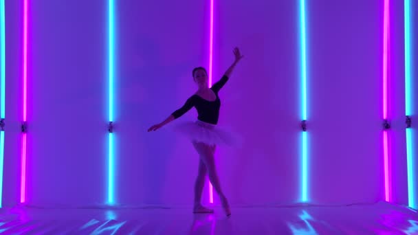 Une ballerine professionnelle effectue des pas de danse sur la pointe des pieds dans le studio sur un fond de tubes néons bleu vif et rose. Chorégraphie d'une ablette classique. Mouvement lent. — Video