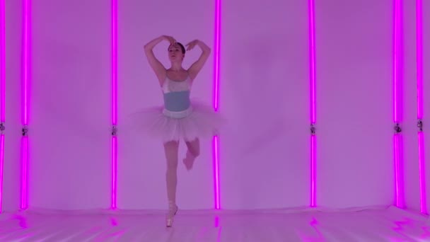 Feminine young graceful ballerina dancing elements of classical ballet. A girl in a stage costume in the studio against the background of multicolored neon tubes. Slow motion. Close up. — Stock Video