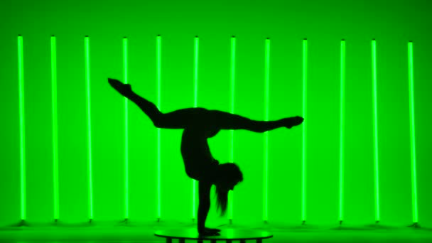 Boční pohled na tmavou siluetu mladé gymnastky ve studiu na pozadí pestrobarevných neonových světel. Dívka dělá stojku ve zpomaleném filmu. — Stock video