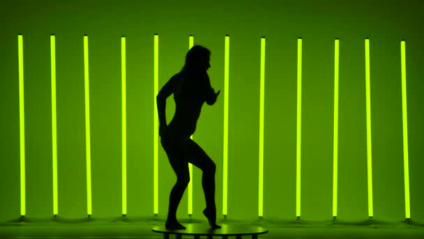 Silueta de una mujer bailando coreografía moderna en el estudio sobre un fondo de tubos de neón. La gimnasta levanta una pierna y hace la división mientras está de pie. Concepto deportivo. De cerca.. — Vídeos de Stock