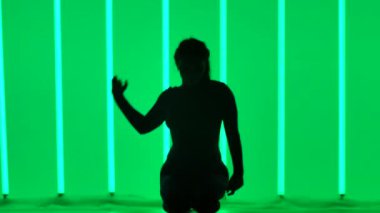 Bir kadın stüdyoda çok renkli neon tüplerin arka planına karşı jimnastik egzersizleri yapıyor. Kız amuda kalkar ve bacaklarını havaya kaldırır. Siluet. Ağır çekim. Kapat..