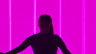 Jimnastikçi stüdyoda neon tüplerin arka planına karşı egzersiz yapar. Kız dirsek duruşu yapıyor, köşeyi dönüyor ve bacaklarını havaya kaldırıyor. Siluet. Ağır çekim. Kapat..