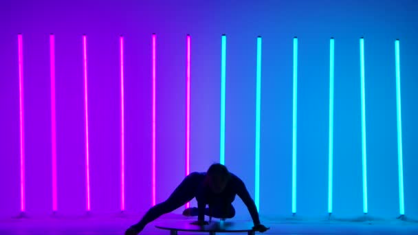 Een aantrekkelijke vrouw voert een handstand, beweegt haar benen en splitst ze in een split. Gymnast in de studio tegen de achtergrond van roze en blauwe neon lichten. Silhouet. Langzame beweging. — Stockvideo