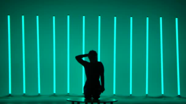 Neon lambaların arka planına karşı bir jimnastikçinin karanlık silueti. Oturma pozisyonundaki bir kız ellerini kaldırır ve bacaklarını kaldırır, onları hareket ettirir, çapraz yapar ve ikiye böler. Yavaş çekim. — Stok video