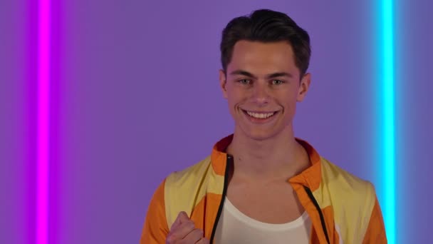 Portrait of stylish guy looking at the camera with excitement then delight celebrating her victory triumph. Male fashion model poses against the backdrop of bright neon lights. Close up. Slow motion. — Stock Video
