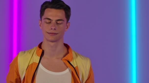 Portrait of stylish guy dancing and enjoying the music. Male fashion model in yellow jacket poses in dark studio against the backdrop of bright neon lights. Close up. Slow motion. — Stock Video