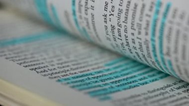 İngilizce metni olan kitabı kapat. Beyaz sayfalar ağır çekimde dönüyor. Bazı çizgiler maviyle vurgulanır, bazıları pembeyle, ana noktaları çabucak bulmak için. Eğitim kavramı.