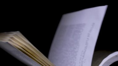 Stüdyoda siyah arka plan üzerine açık bir kitap. Bulanık metinli sayfalar yavaş çekimde çevriliyor. Kapat..
