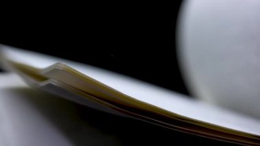 Stüdyoda siyah arka plan üzerine açık bir kitap. Bulanık metinli sayfalar yavaş çekimde çevriliyor. Kapat..