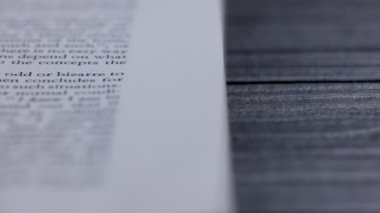 Üzerinde İngilizce metin olan açık bir kitap ahşap bir masanın üzerinde yatıyor. Kitabın sayfaları ağır çekimde döndü. Metnin bir kısmı bulanık. Kapat..