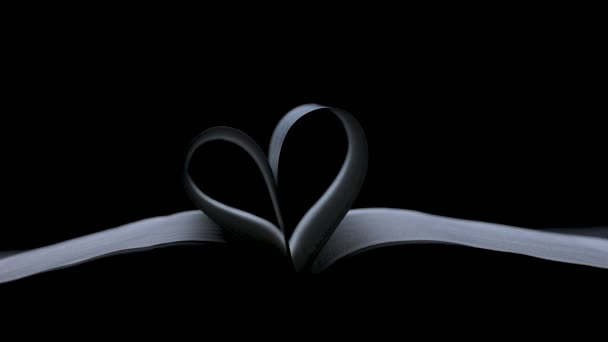 An open book lies in a dark studio on a black background. The pages of the book are folded in the shape of a heart. Valentines day concept. Slow motion. Close up. — Stock Video