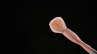 Kremsi makyaj fırçası ürker ve yavaş çekimde siyah bir zemine karşı ince pembe toz zerreleri oluşturur. Güzellik salonu, güzellik mağazası. Kapat..