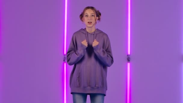 Retrato de una joven mujer atractiva mirando a la cámara con emoción y luego deleitarse celebrando su triunfo de la victoria. Modelo de moda posa sobre fondo de luces de neón brillantes. Movimiento lento. — Vídeo de stock