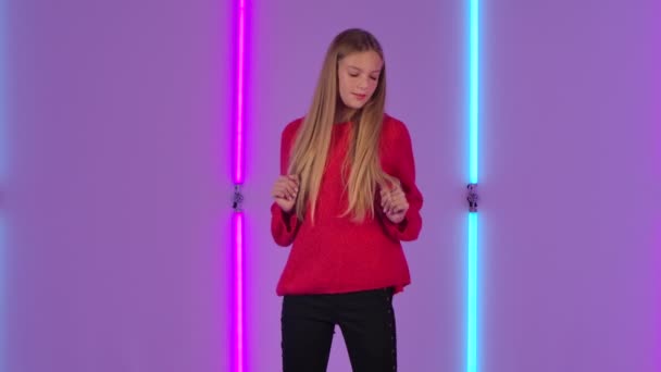 Porträt einer jungen, charmanten Frau, die für die Kamera tanzt und posiert. Modemodel mit langen Haaren im roten Pullover vor hellem Neonlicht im dunklen Studio. Zeitlupe. — Stockvideo