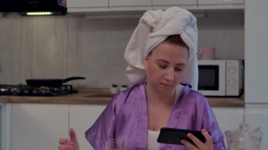 Kadın mutfakta oturmuş telefona bakıyor, konuşuyor. Aman Tanrım, zaferi kutluyor, iyi haberler alıyor. Kafasında havlu olan kadın, arka plandaki ışık odasına karşı duruyor. Kapatın. Yavaş çekim.