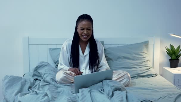 Güzel bir Afro-Amerikalı kadın, portatif bir dizüstü bilgisayar kullanarak görüntülü konuşma yapıyor. Gücenmiş ve kızgın. Siyah kadın pijamalarıyla yatak odasında poz veriyor. Odanın içi aydınlık. Yavaş çekim. — Stok video