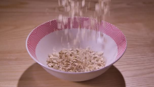 Torr havregryn faller ner i en vit röd tallrik. Ekologisk och dietfrukost. Rätt och hälsosam kost. Matlagning i hemköket. Närbild. Långsamma rörelser. — Stockvideo