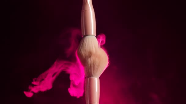 Two makeup brushes touch each other to form an intricate swirl of cosmetic powder particles. Close up of makeup brushes in a dark studio in bright red neon light. Slow motion. — Stock Video