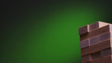 Yeşil gradyan üzerinde Jenga oyunu. Kızlar yavaş çekimde kuleye bir blok bildiriyor. Kamera hareketi soldan sağa doğru. Kapat..