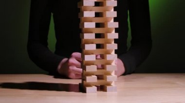 Kız yeşil bir arkaplanda Jenga masa oyunu oynuyor. Kız onlardan birini çıkardığında tahta bloklardan bir kule düşer. Kamera sağdan sola hareket ediyor. Ağır çekim. Kapat..