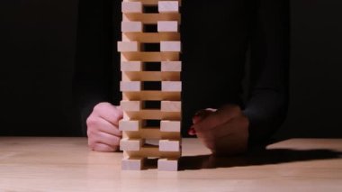 Kız yeşil bir arkaplanda Jenga masa oyunu oynuyor. Kız onlardan birini çıkardığında tahta bloklardan bir kule düşer. Kamera hareketi soldan sağa doğru. Ağır çekim. Kapat..