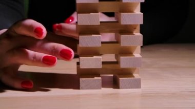 Bir kadın eli ahşap bir tuğla çıkarır ve bina çöker. Jenga Kulesi masaya ağır çekimde çarpıyor. İş riskleri. Kapat..