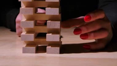 Bir kadın eli ahşap bir taş çıkarır ve kule çöker, masaya tahta tuğlalar saçılır. İş riskleri. Jenga masaya düşer. Ağır çekim. Kapat..