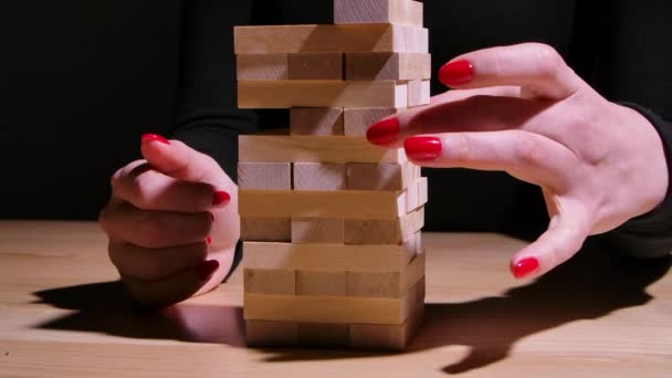 A menina habilmente joga Jenga enquanto se senta na mesa. As mãos meninas cuidadosamente remover os blocos de madeira e colocá-los no topo da torre sem destruí-lo. Movimento lento. Fechar. — Vídeo de Stock