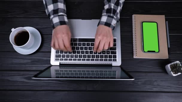 Førsteklasses bilde av hendene til en jente som skriver e-post på en bærbar PC. Nær laptopen er det en smarttelefon med grønn skjerm og en kromnøkkel. Plass for reklameinnholdet. Langsom bevegelse. Lukk. – stockvideo