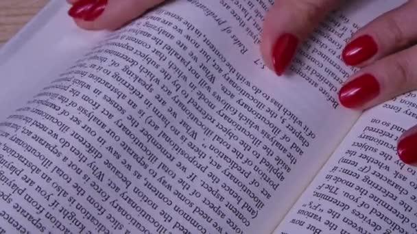 Una donna legge un libro aperto. Girando le pagine con le mani, la ragazza si ferma a quella desiderata. Concetto educativo. Al rallentatore. Da vicino.. — Video Stock