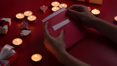 Womans hands open envelope and take out a valentine card with inscription love you. Top view of red table with burning candles, decorative hearts and gift. Valentines Day. Close up. Slow motion.